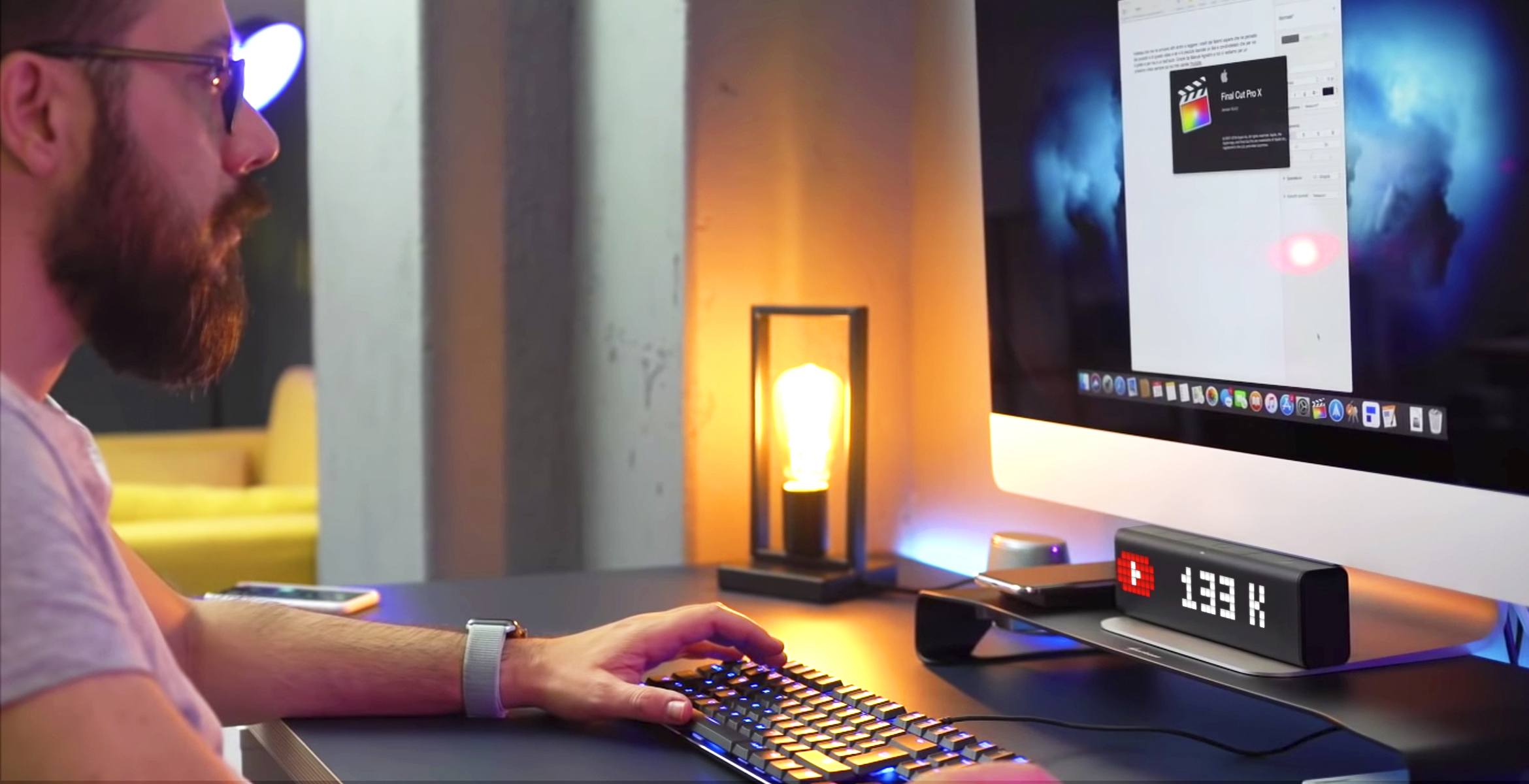 A Youtuber creating his new video on the computer and smart clock displaying his subscribers count for the YouTube